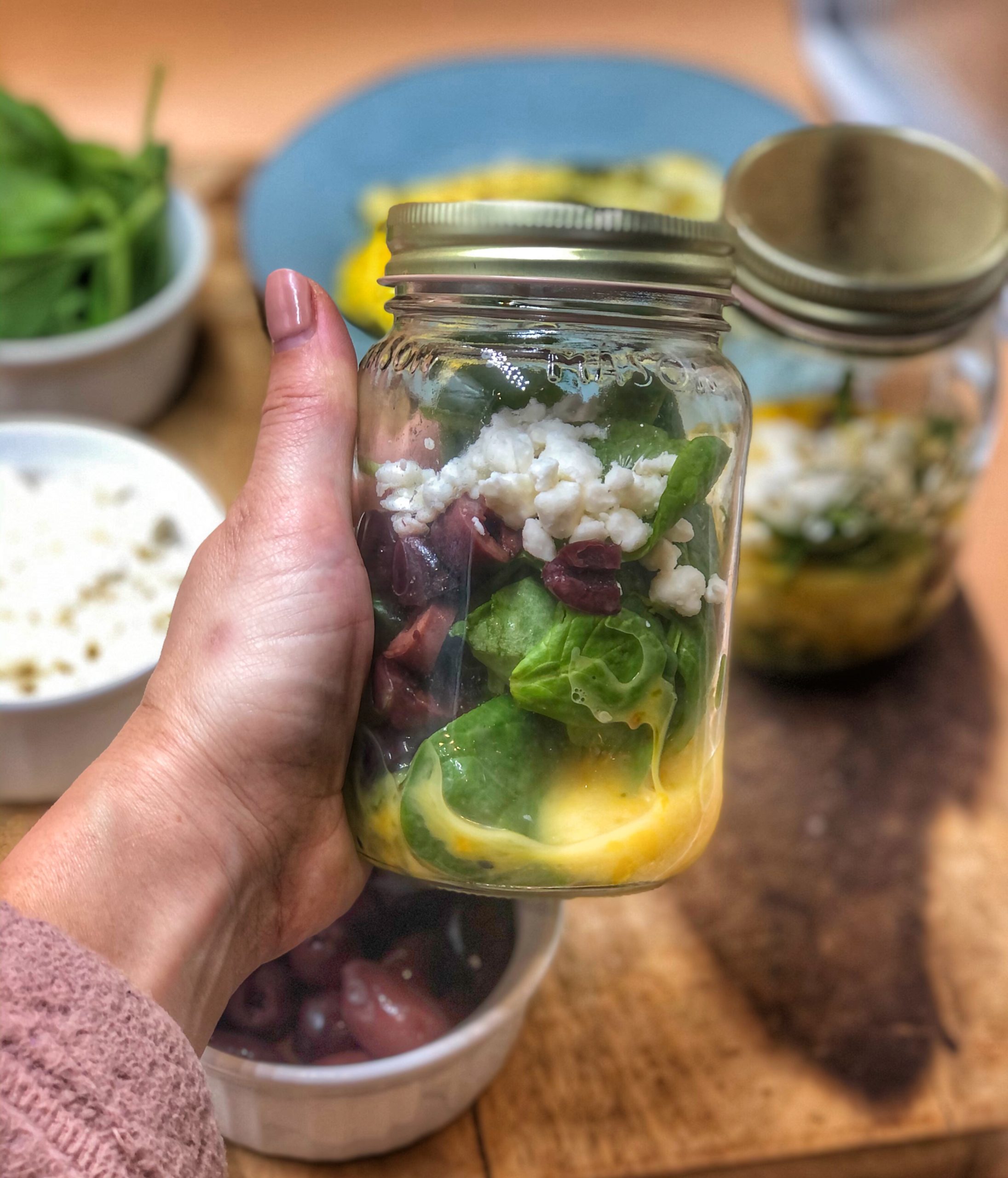 a hand holding a breakfast jar with a greek omelette inside