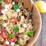 A birds eye view of a Caprese Pasta Salad in a wooden bowl with fresh basil scattered on top.