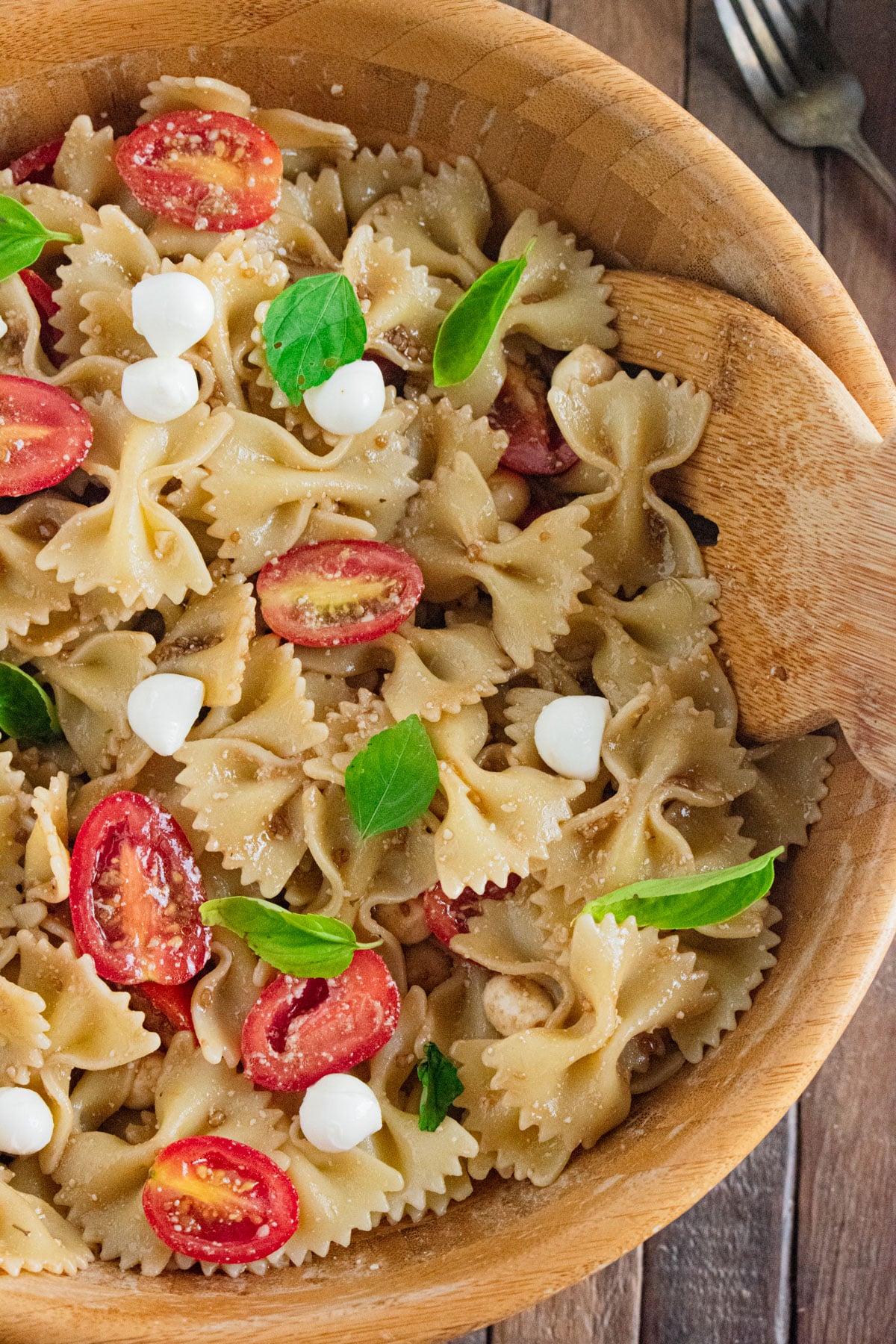 A close up of Caprese Pasta Salad in a wooden bowl with fresh basil scattered on top.