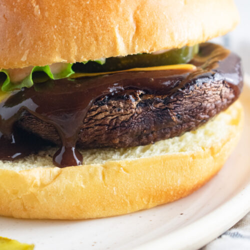 Close up of portobello mushroom burger on a bun with sauce oozing over top.