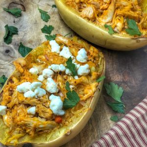 close up of buffalo chicken spaghetti squash on a wooden board with a stripped towel