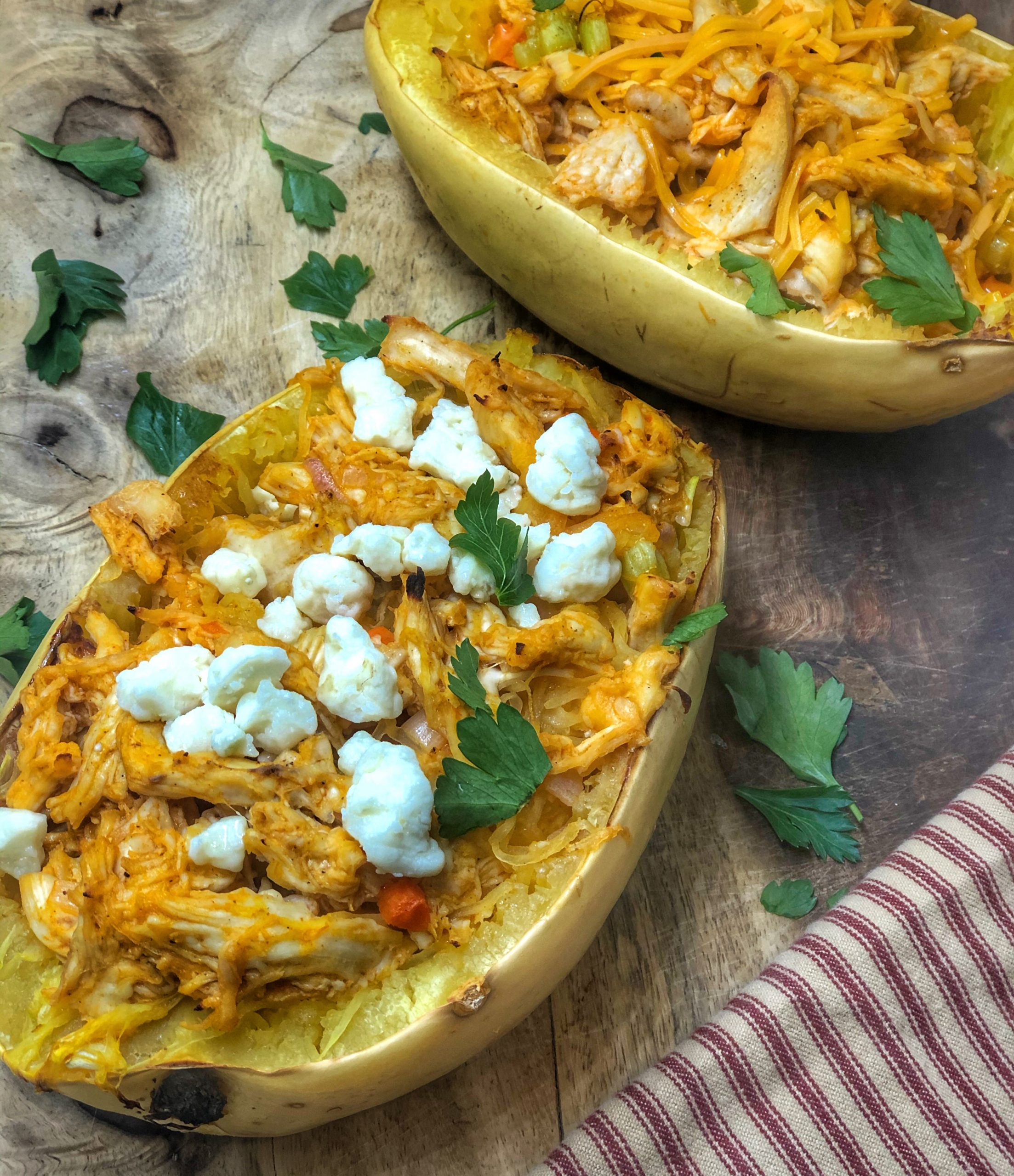 close up of buffalo chicken spaghetti squash on a wooden board with a stripped towel