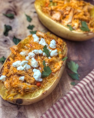 close up of buffalo chicken stuffed spaghetti squash on a wooden board with a stripped towel