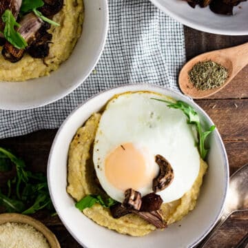 Polenta in a white bowl topped with sliced mushrooms and a fried egg.