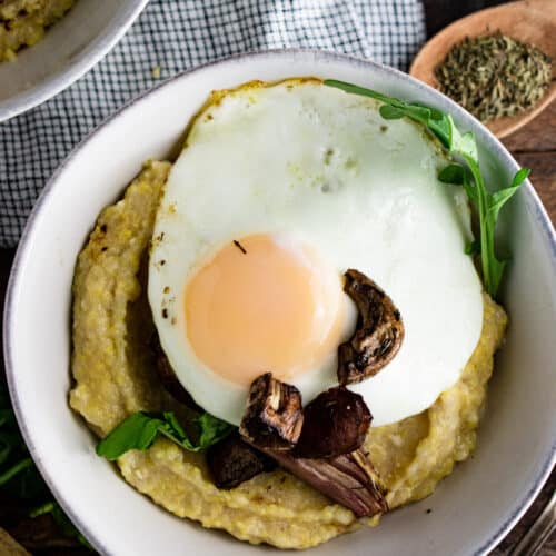 Polenta in a white bowl topped with sliced mushrooms and a fried egg.
