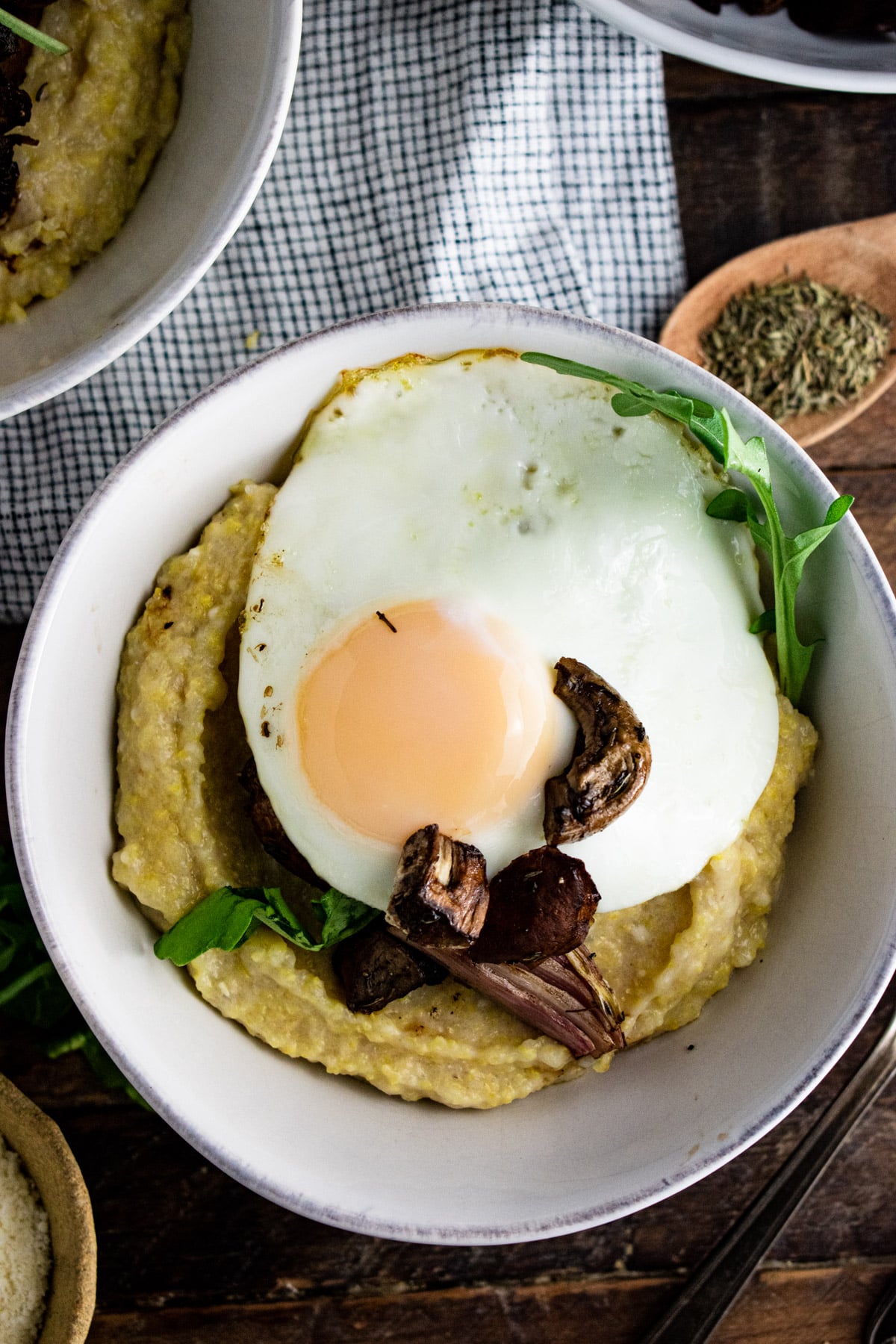 Polenta in a white bowl topped with sliced mushrooms and a fried egg.