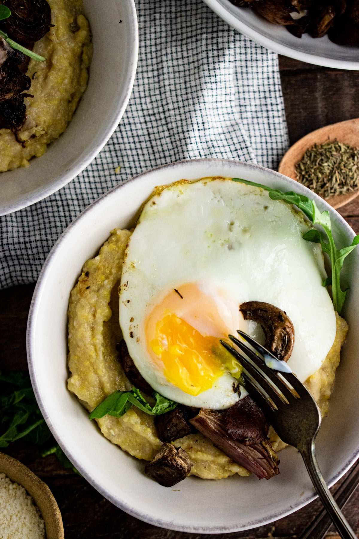 Polenta in a white bowl topped with sliced mushrooms and a fried egg.