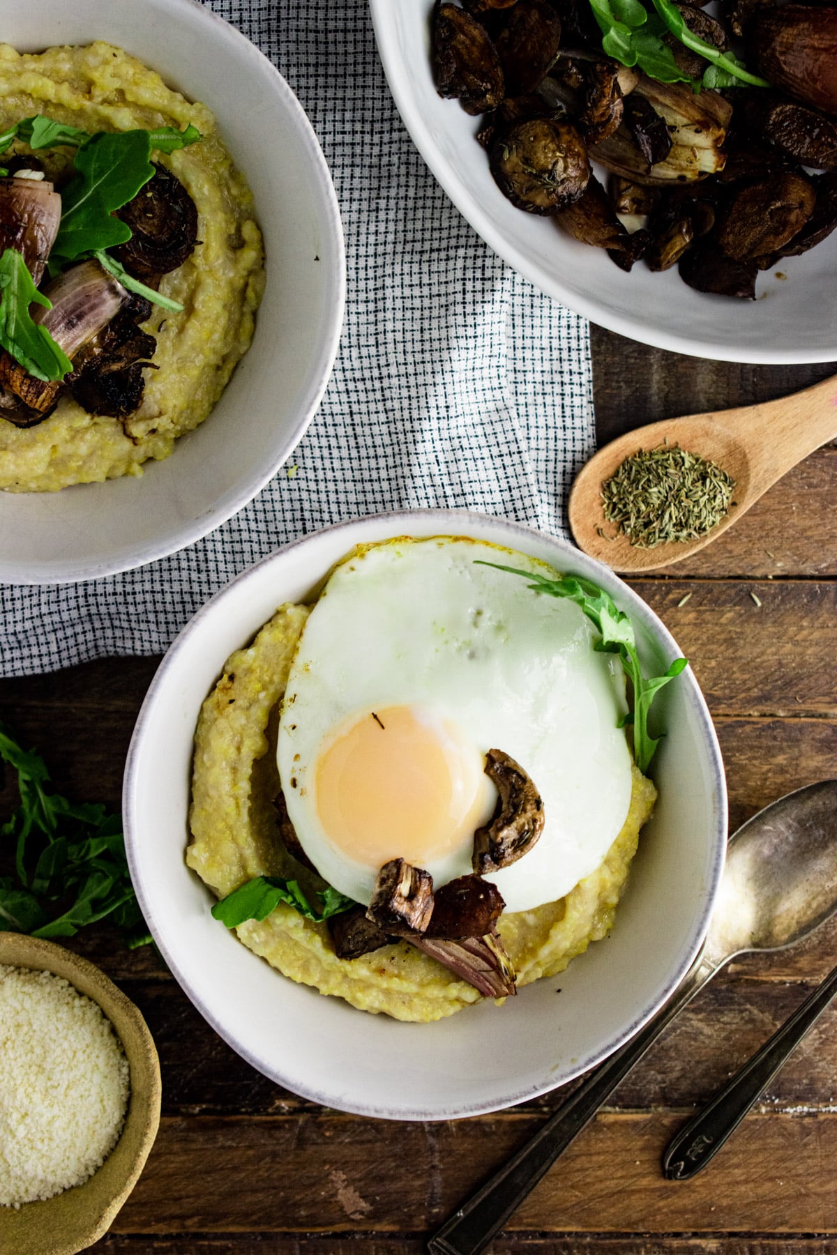 Polenta in a white bowl topped with sliced mushrooms and a fried egg.