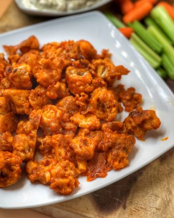 buffalo cauliflower bites on a white plate with blue cheese and celery