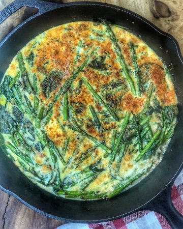 green frittata in a cast iron skillet on a wooden cutting board