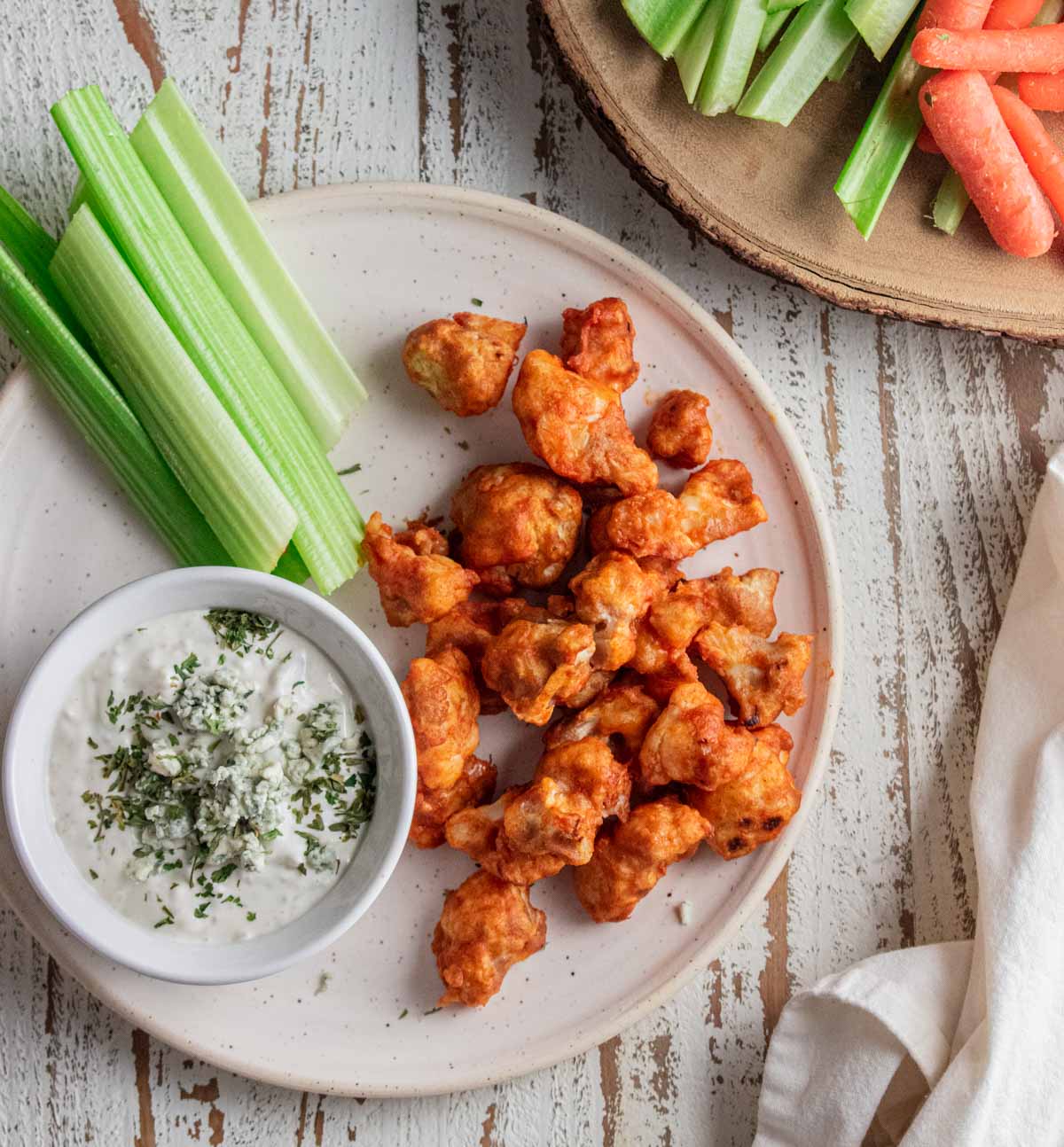 birds-eye view of buffalo cauliflower bites on a white plate with blue cheese and celery stalks 