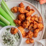 birds-eye view of buffalo cauliflower bites on a white plate with blue cheese and chopped cauliflower stalks