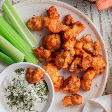 birds-eye view of buffalo cauliflower bites on a white plate with blue cheese and chopped cauliflower stalks