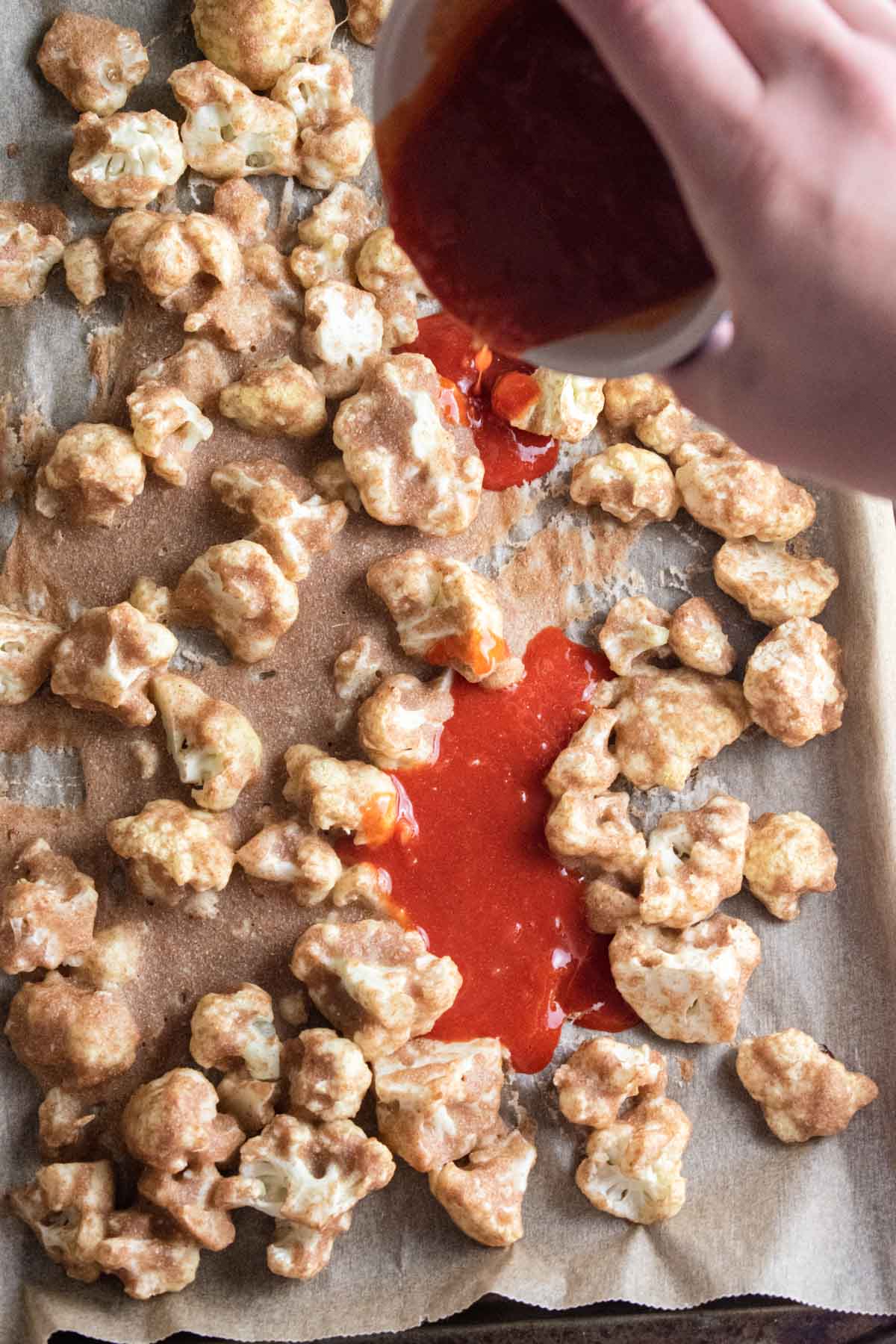 cauliflower on a baking pan having buffalo sauce being poured over top