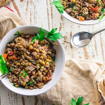 a birds eye view of ground turkey lentil soup in a white bowl topped with fresh parsley on a wooden board