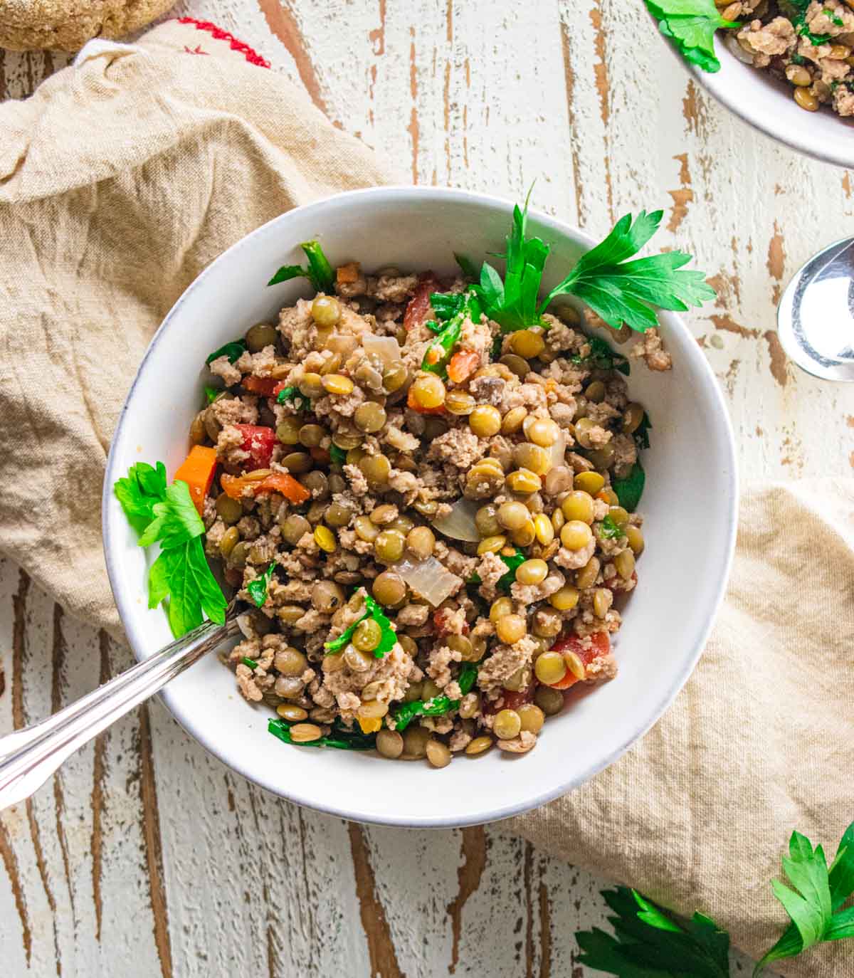 ground turkey lentil soup in a white bowl topped with fresh parsley sitting on a white wooden board