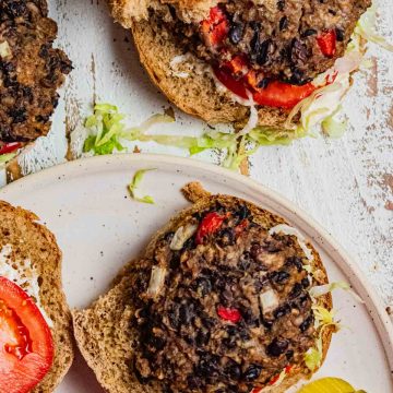 birds eye view of homemade easy black bean burgers on a whole wheat bun with tomato slices, shredded lettuce, and a side of pickles