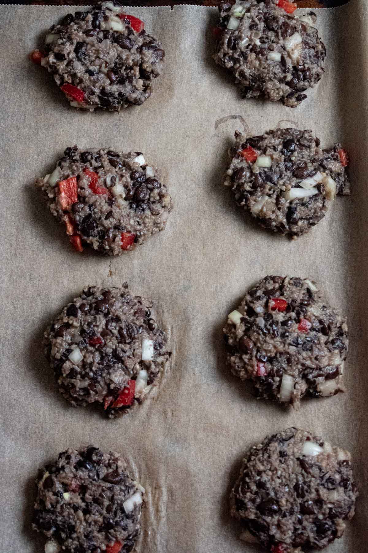 8 black bean burgers lined on a baking tray with parchment paper