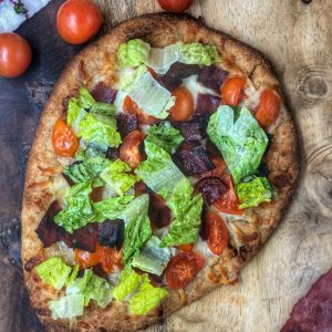 blt naan pizza on a wooden board with tomatoes and turkey bacon next to it