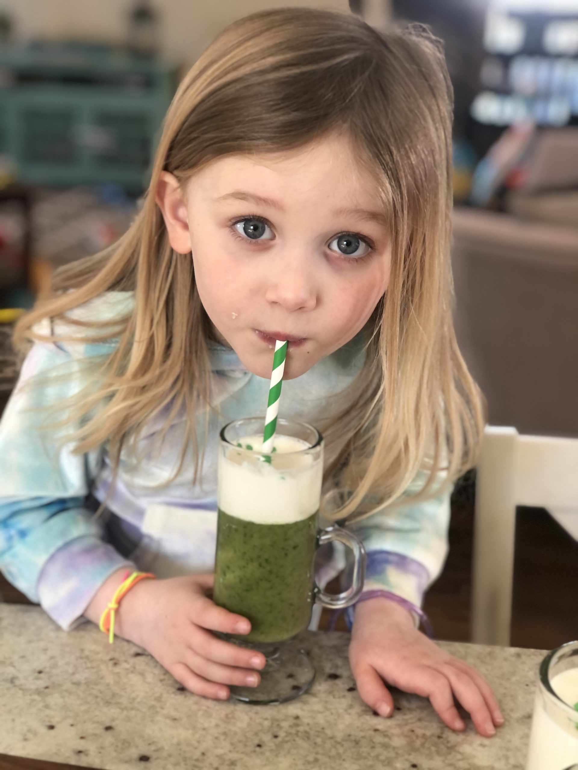 little blonde girl drinking a healthy shamrock shake with a green and white paper straw