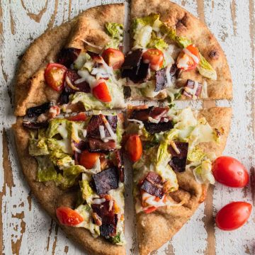 birds eye view of a bacon lettuce and tomato naan bread pizza on a white wooden board