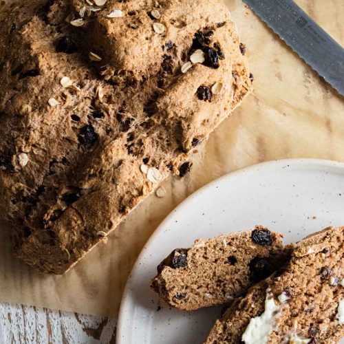 irish soda bread on a piece of parchment paper with a slice next to the loaf with butter on it