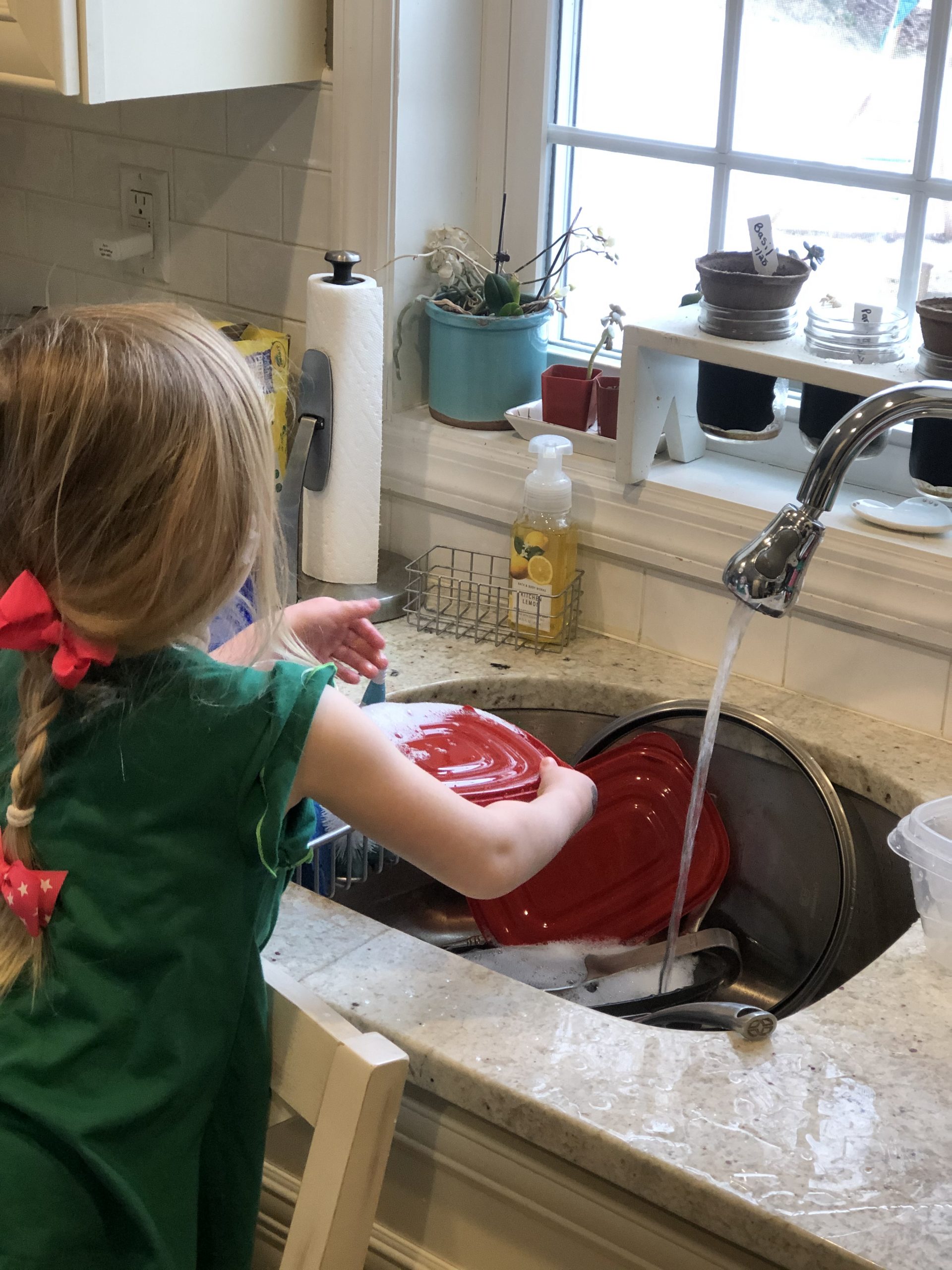 Blonde girl doing the dishes with a pink bow in her hair.