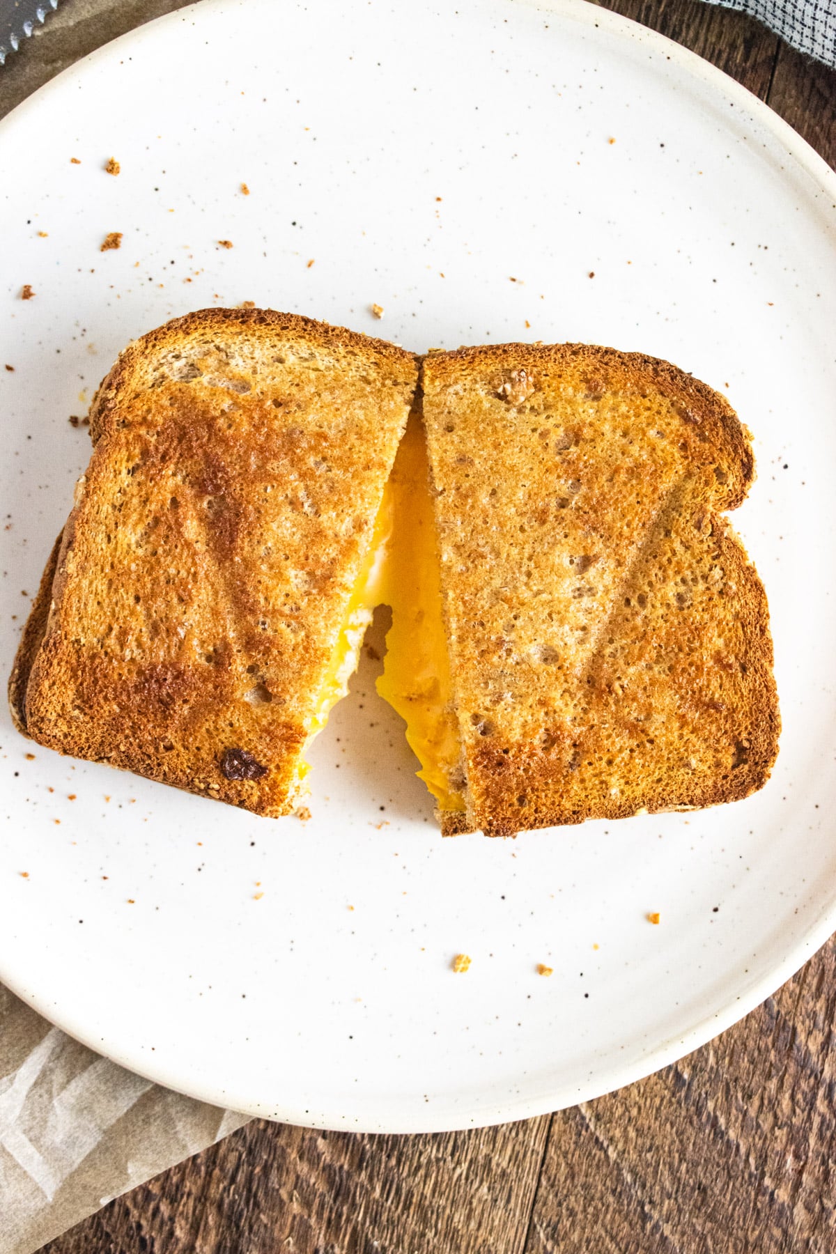 A close up of air fryer grilled cheese on a white plate with the melted cheese oozing between the two pieces of crispy bread.