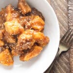 Homemade sweet adn sour chicken in a white bowl on a wooden board.