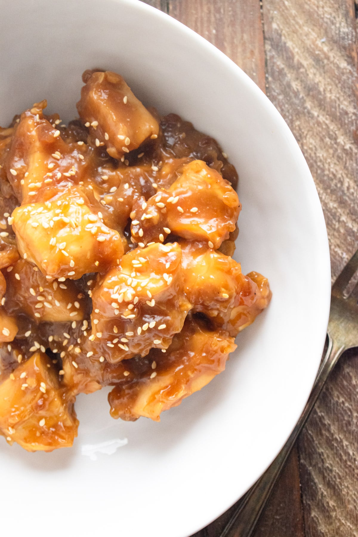 Homemade sweet and sour chicken in a white bowl on a wooden counter.