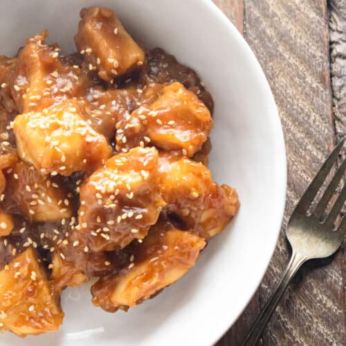 Sweet and sour chicken in a white bowl topped with sesame seeds.