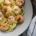 A close up of garlic butter shrimp pasta in a white bowl with a striped napkin next to it.
