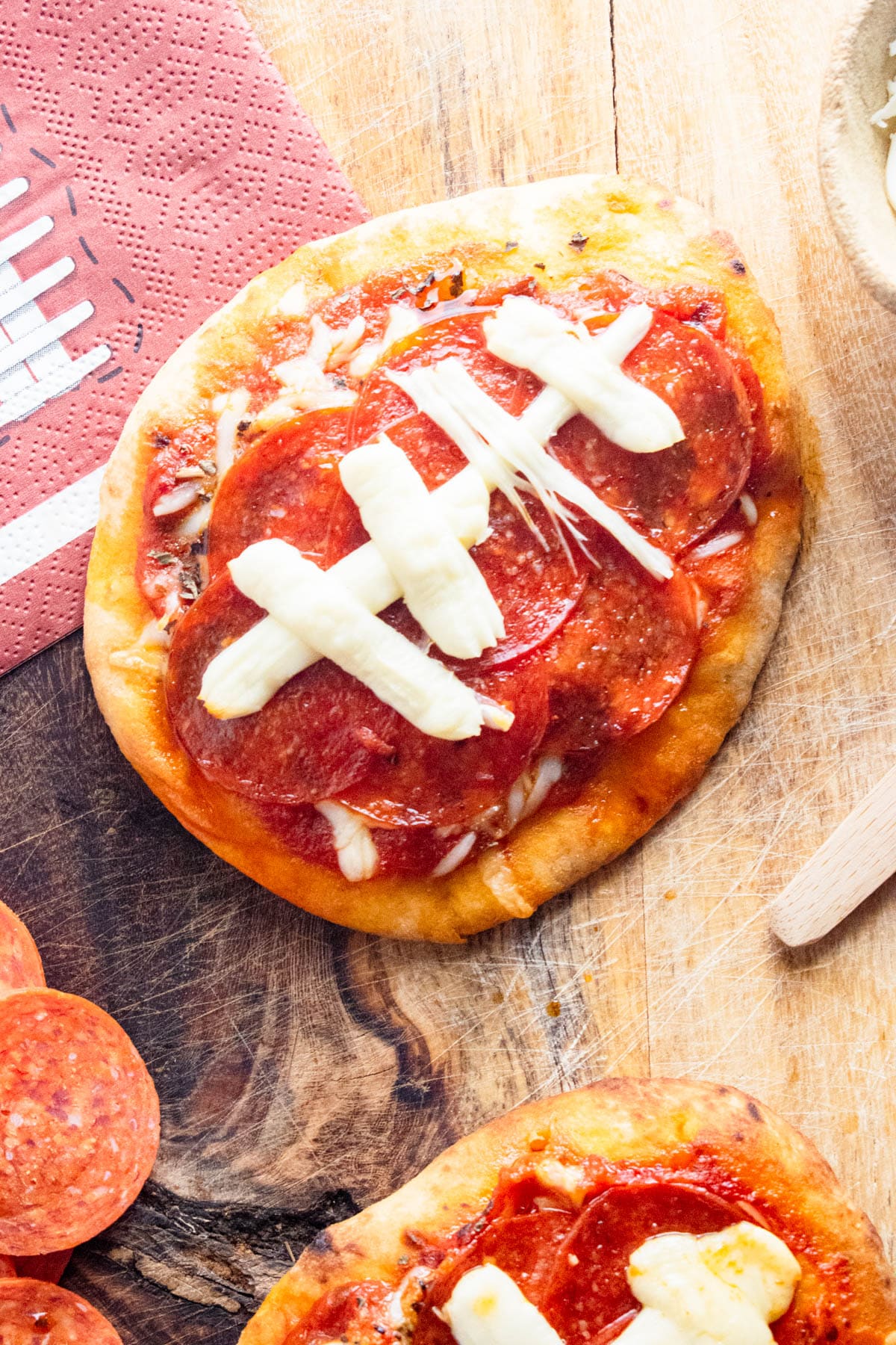 Closeup of football shaped naan pizza on a wooden table with football napkins.