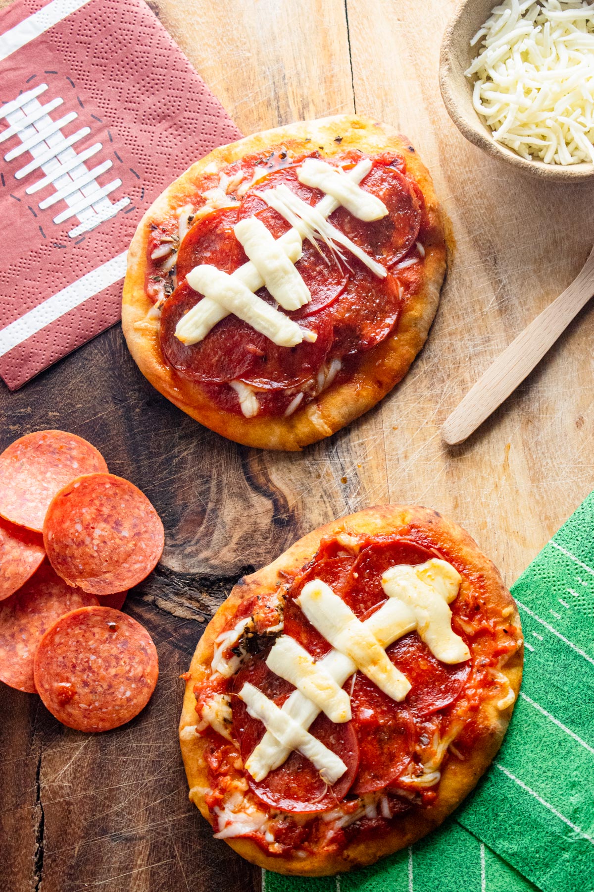 Two football shaped pizzas with pepperoni on the side and football napkins.
