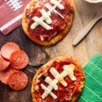 Football shaped Naan bread pizzas on a wooden table with football napkins.