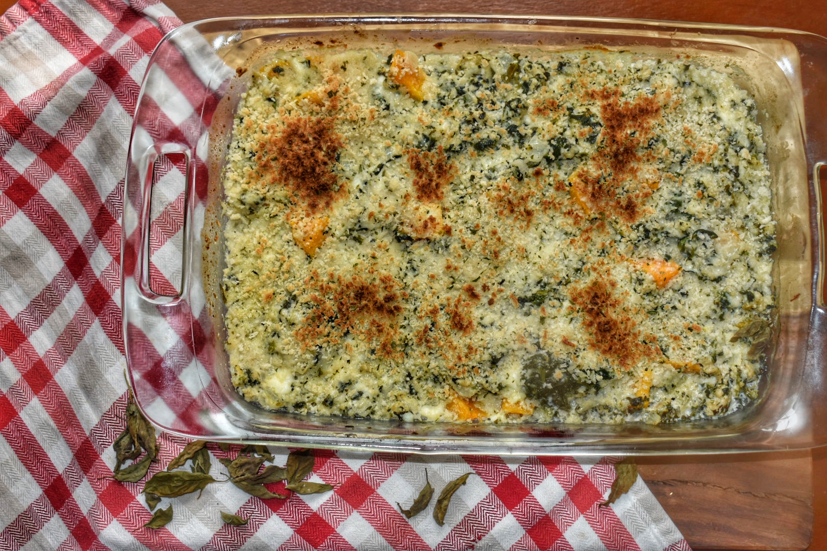 birds eye view of cheesy squash gratin in a glass baking dish on a red and white checkered napkin