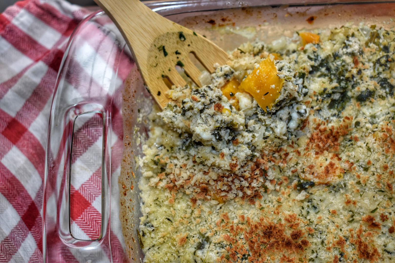 close up of cheesy squash gratin being spooned out with a wooden spoon