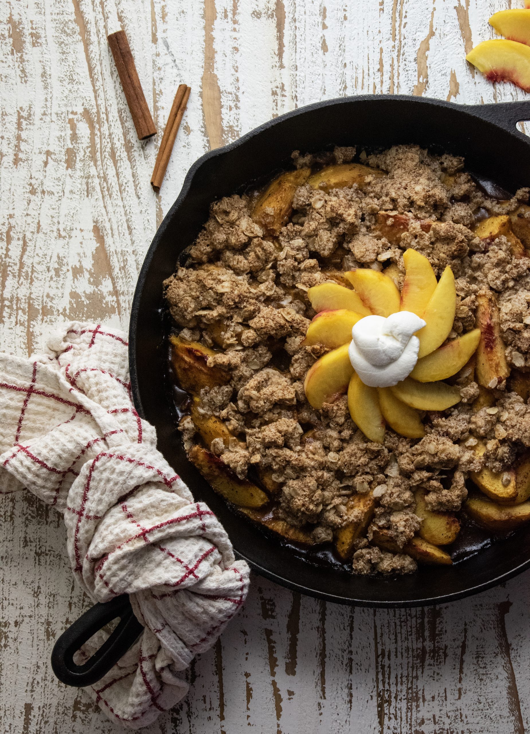 healthy peach crisp in a cast iron skillet on  a white wooden cutting board