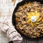 healthy peach crisp in a cast iron skillet on a white wooden cutting board