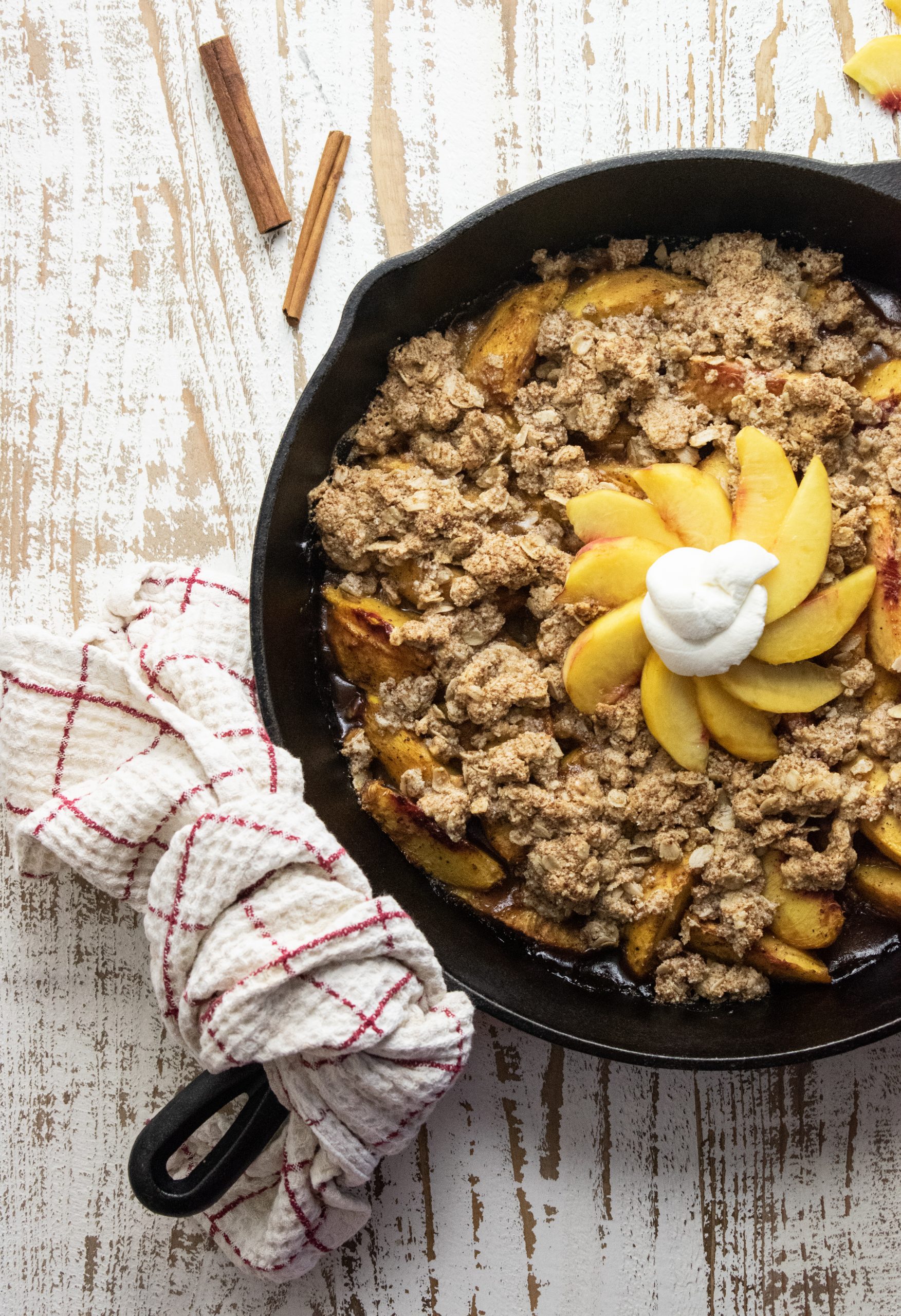 healthy peach crisp in a cast iron skillet on a white wooden cutting board