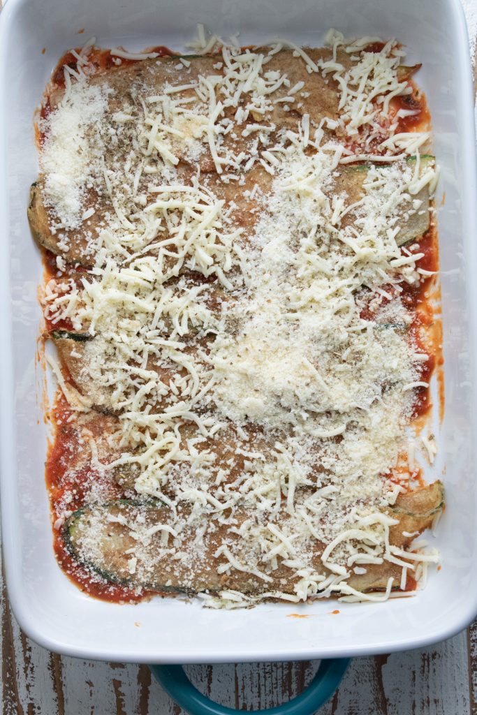 shredded mozzarella cheese laid on top of strips of fried zucchini in a 9 x 13 inch baking dish