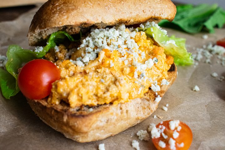 a close up of buffalo ground chicken sloppy joes on toasted buns with crumbled blue cheese on top cherry tomatoes and romaine lettuce