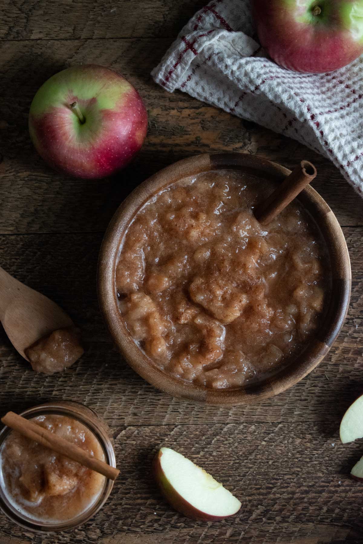 homemade crockpot applesauce sitting in a wooden bowl on a wooden table with apples scattered around