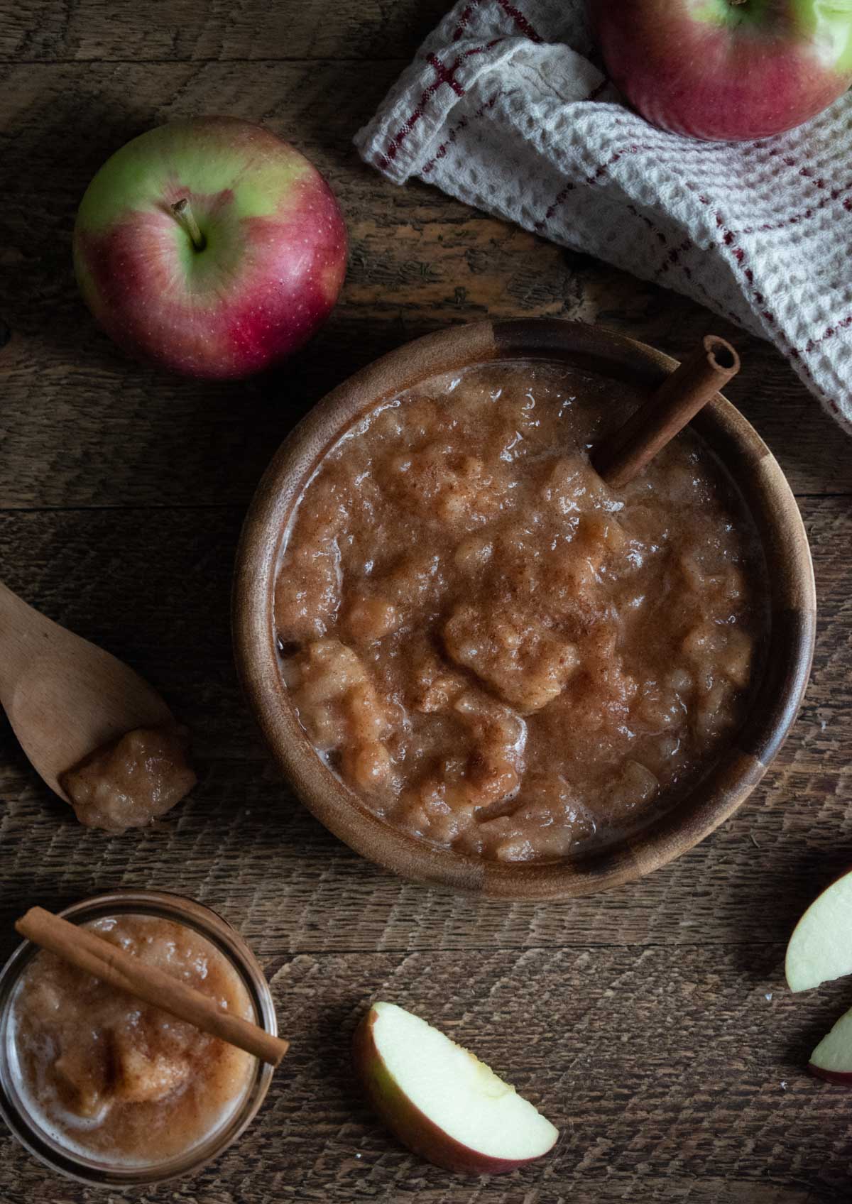 homemade-crockpot-applesauce in a wooden bowl on a wooden table with apples scattered around 