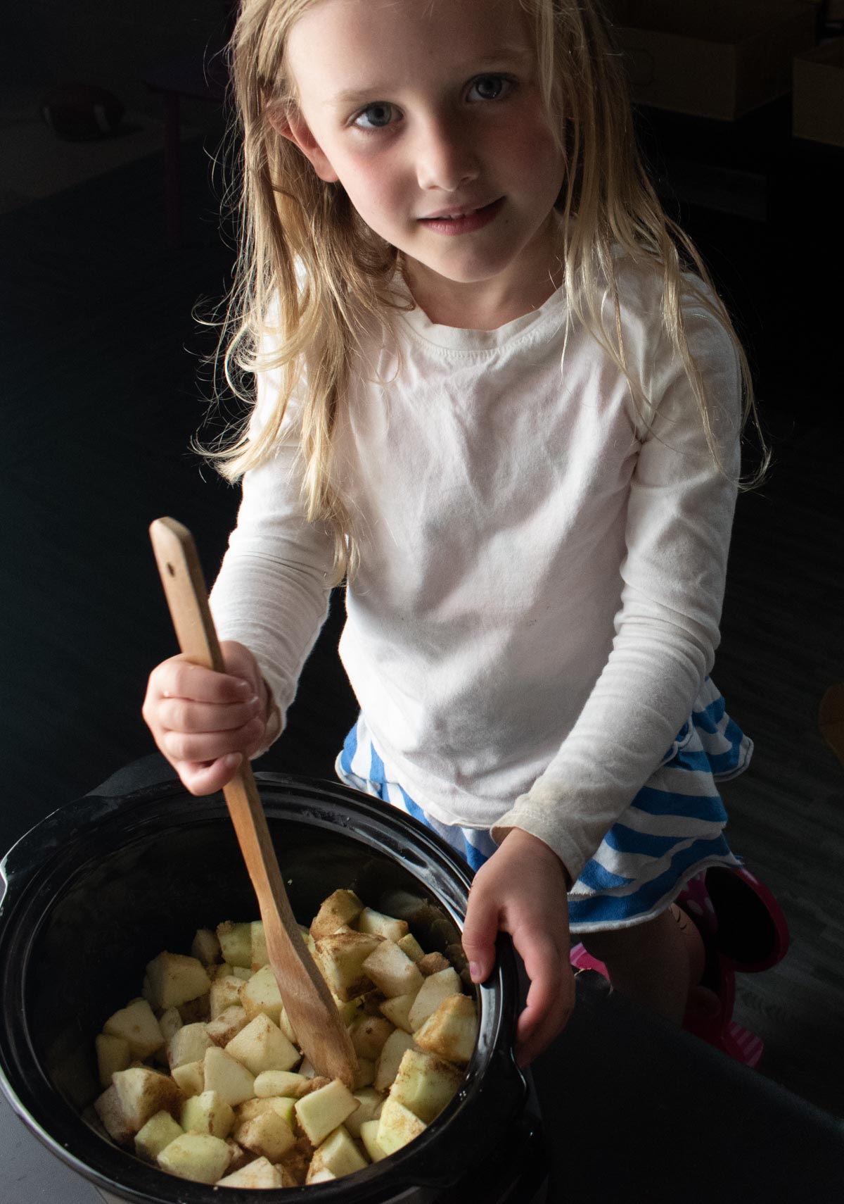 little blonde girl stirring homemade crockpot applesauce with a wooden spoon