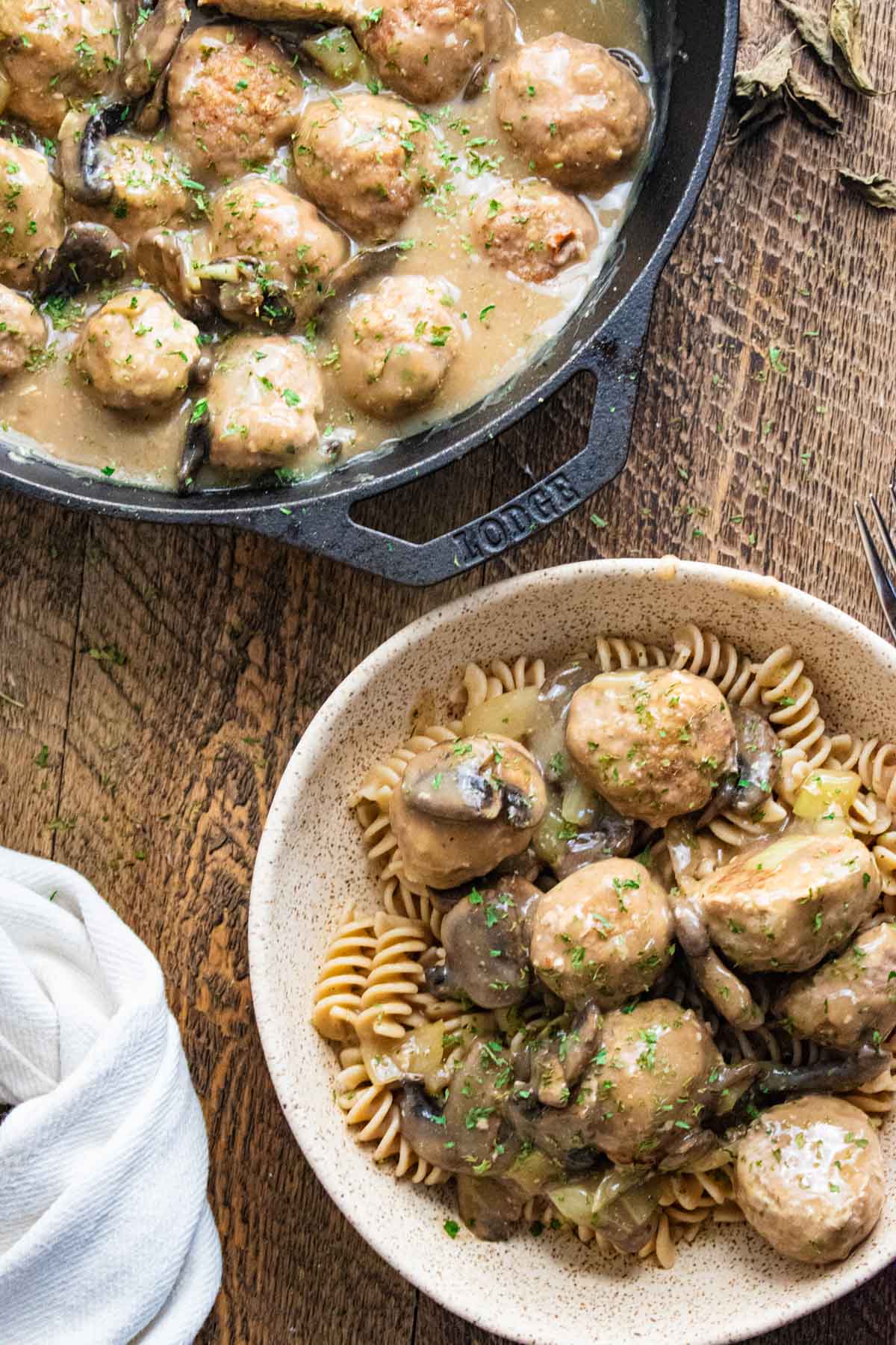 Swedish meatball stroganoff in a cast iron skillet with a bowl of pasta and a creamy mushroom sauce