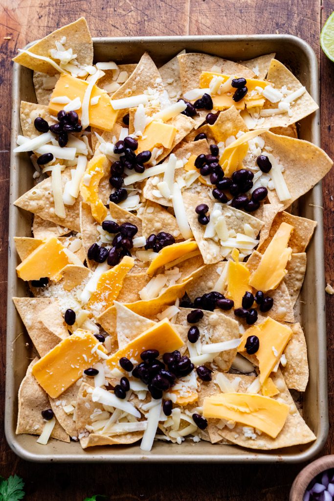 tortillas lined on a baking tray with cheese and black beans