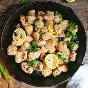 garlic butter chicken bites in a cast iron skillet topped with lemon slices and fresh parsley