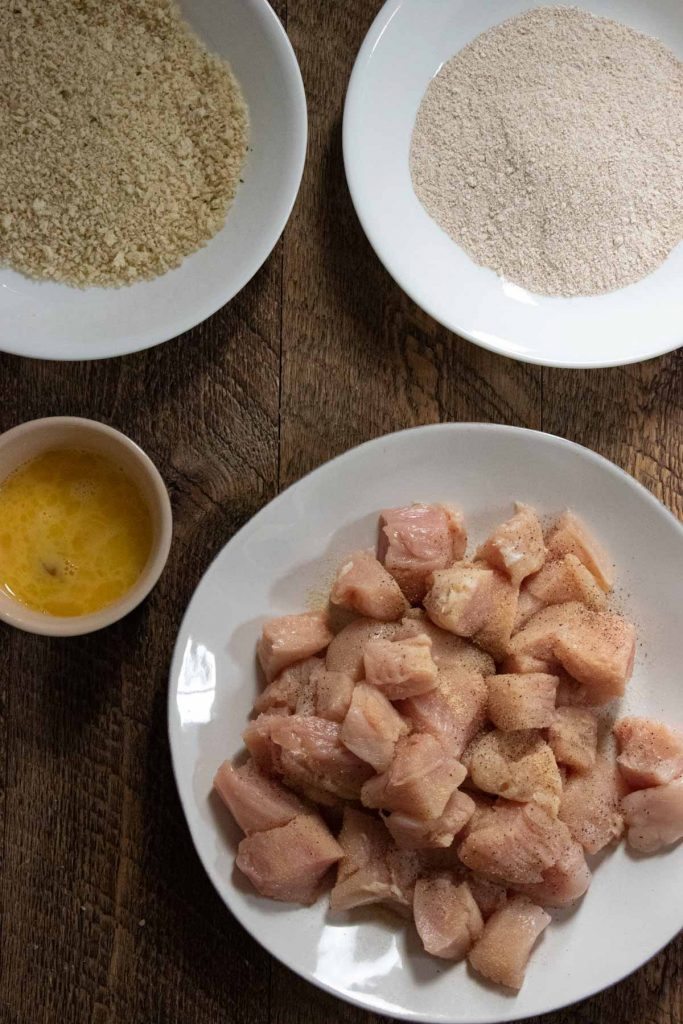 bite sized chicken pieces in a bowl with an assembly line to create garlic chicken bites