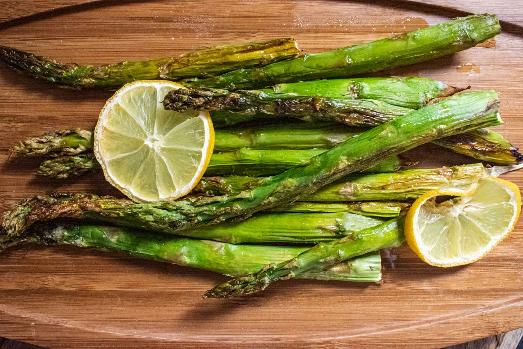 close up of lemon asparagus topped with lemon slices on a wooden board